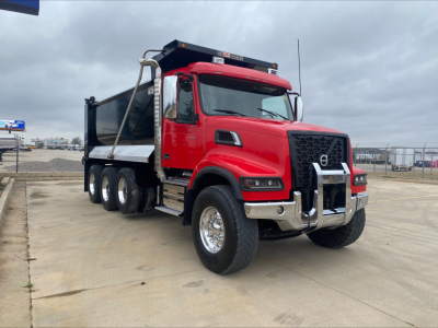 Volvo VHD84F200 dump truck showing red cab and black dump bed with chrome bumper and guard, front three-quarter view.
