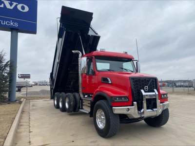 Volvo VHD84F200 dump truck with raised bed, red cab, chrome bumper, black dump body, showing front three-quarter view.