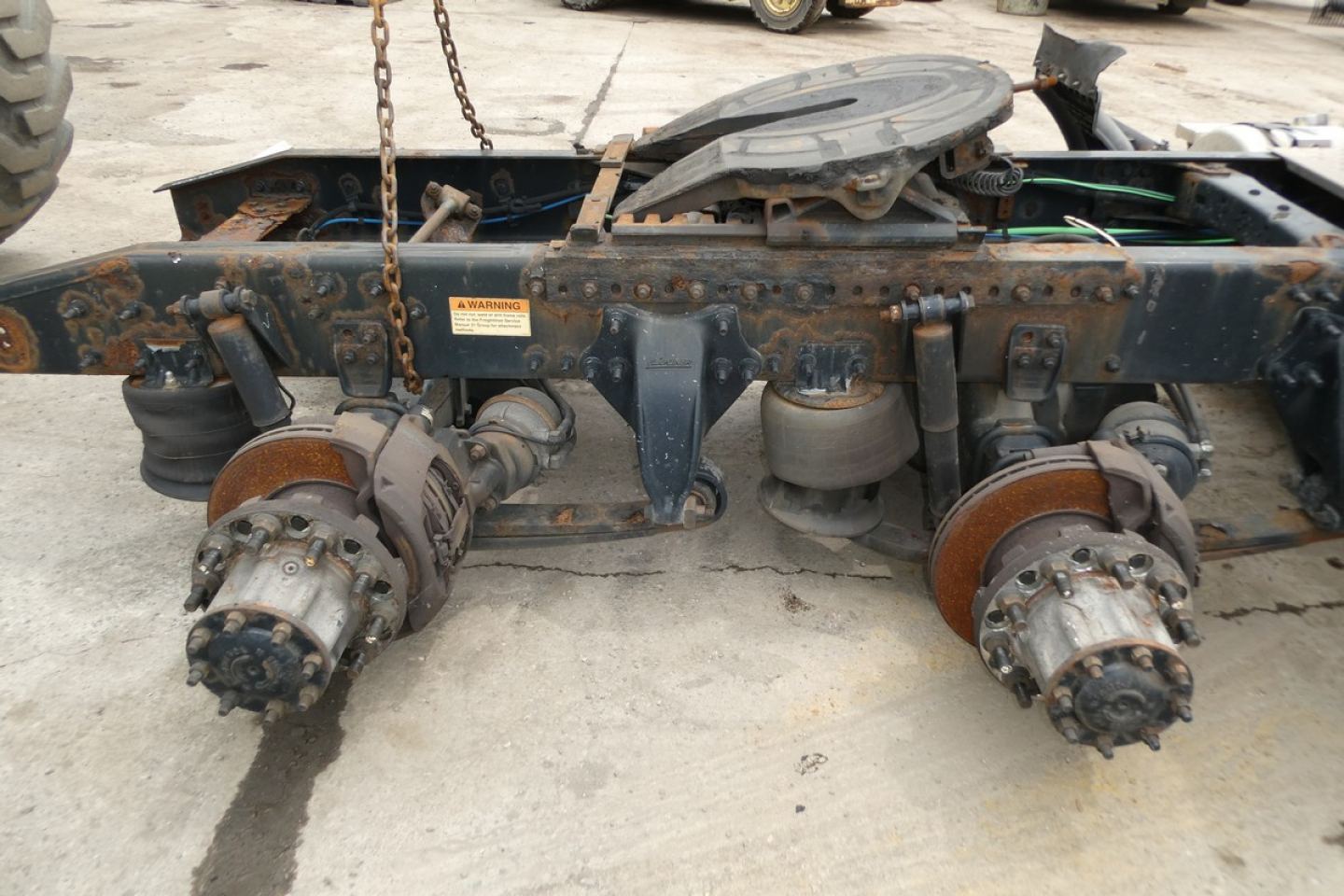 Freightliner Cascadia 125 chassis rear view showing hub assemblies and brake components with rust and debris, undercarriage with chain and fuel tank cap visible.