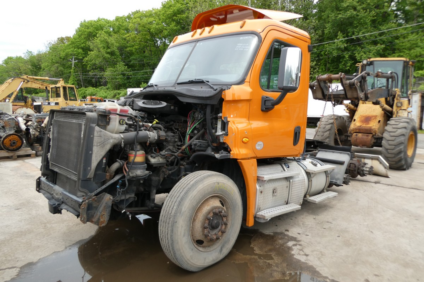 Truck engine bay view of a 2017 Freightliner Cascadia 125 conventional daycab, orange cab, exposed engine components at front with radiator and hoses visible.