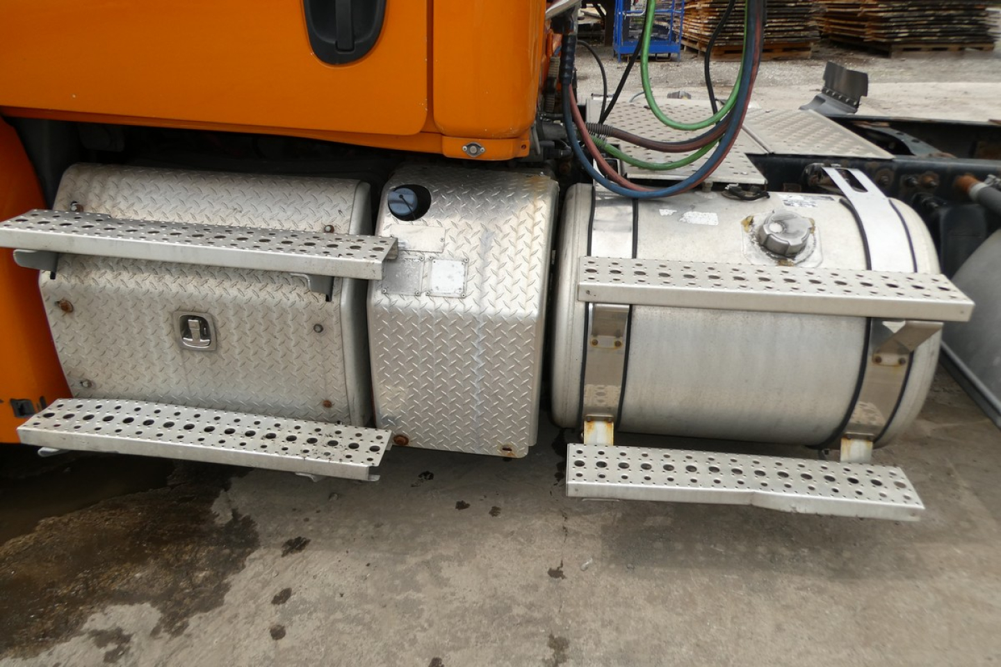 Fuel tanks and side steps of a Freightliner Cascadia 125 tractor showing aluminum RH fuel tank with diamond plate toolbox and steps, orange cab visible.