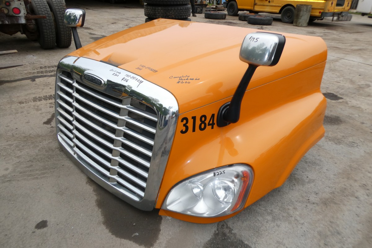 Truck hood and grille of a 2017 Freightliner Cascadia 125 daycab showing orange paint, chrome grille, side mirror, and headlight assembly with number 3184.