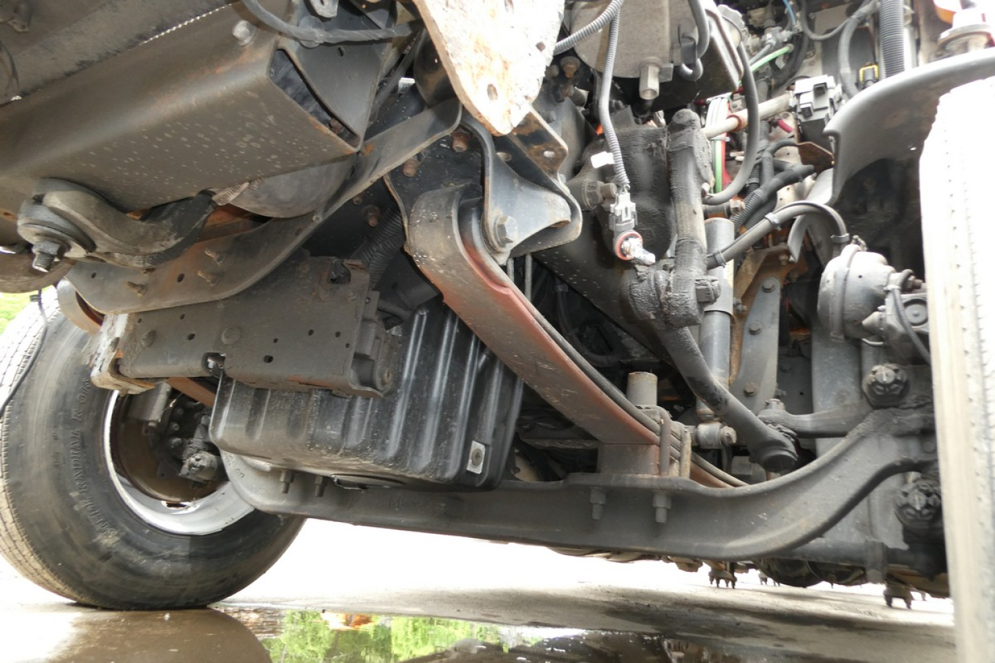 Underbelly of a Freightliner Cascadia 125 showing engine components, wiring, and frame with visible metal brackets and hoses.