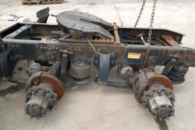 Truck rear chassis with fifth wheel and two air brake/drive wheel assemblies exposed, rust and grime on components, Freightliner Cascadia 125 chassis area, visible warning label.