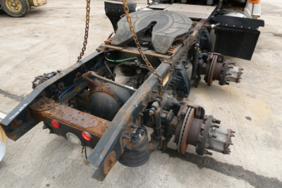 Rear frame of a Freightliner Cascadia chassis showing brake components, axles, and rusty frame with chains and a removed cab area.