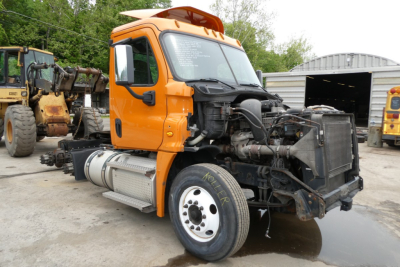 Orange Freightliner Cascadia 125 daycab truck with missing front hood and exposed engine bay, side view showing front left wheel and exhaust tank.