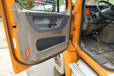 Truck cab interior door panel and driver seat area of a 2017 Freightliner Cascadia 125 conventional daycab showing open door and steering wheel.