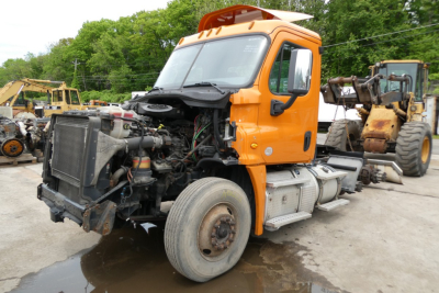 Truck engine bay view of a 2017 Freightliner Cascadia 125 conventional daycab, orange cab, exposed engine components at front with radiator and hoses visible.