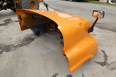Orange truck cab front fender and mirror assembly detached from Freightliner Cascadia 125 showing wheel well and frame.