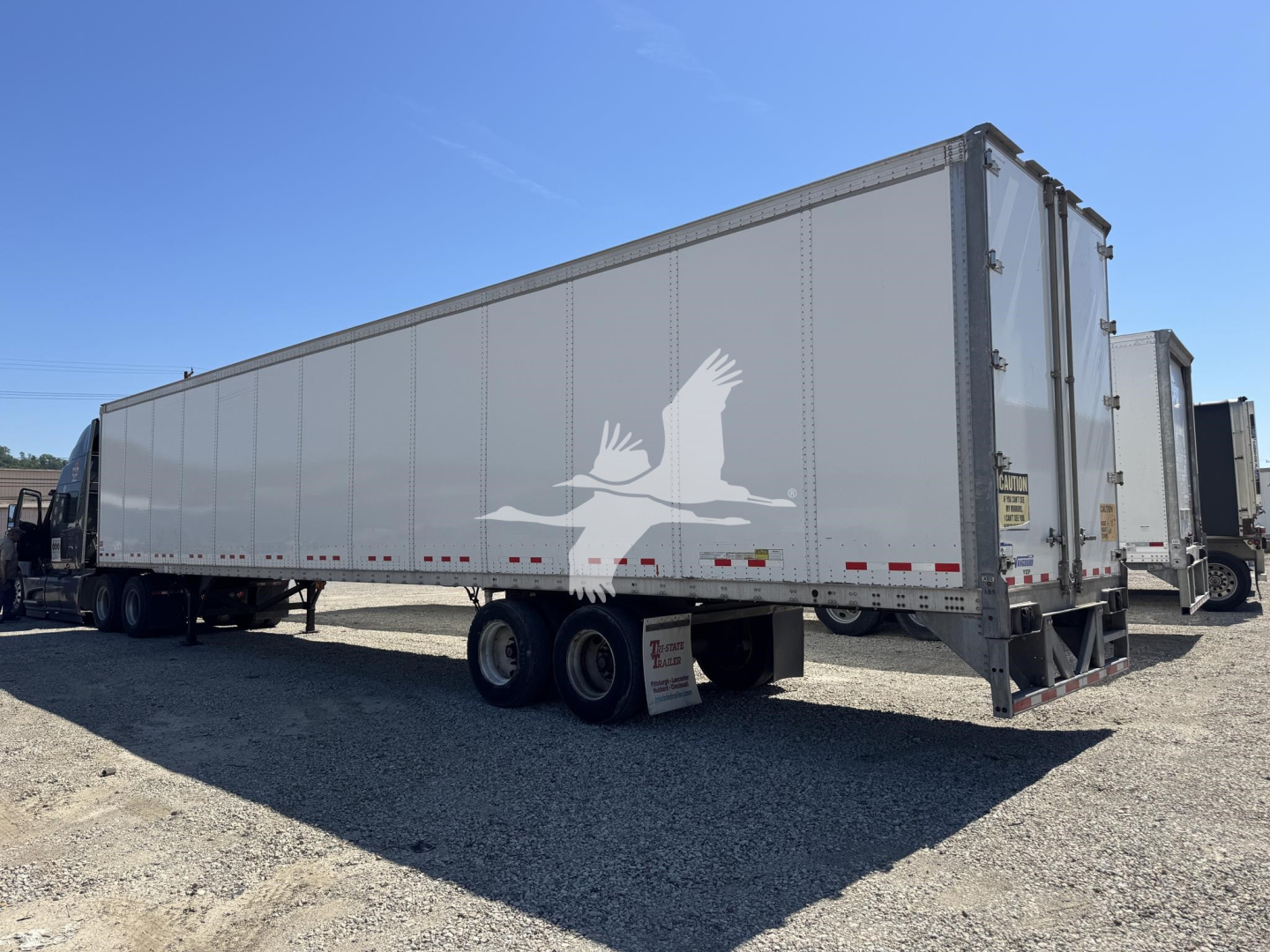 Trailer side view showing a large enclosed gooseneck trailer with Vanguard logo and side panels, no visible labels readable from distance.