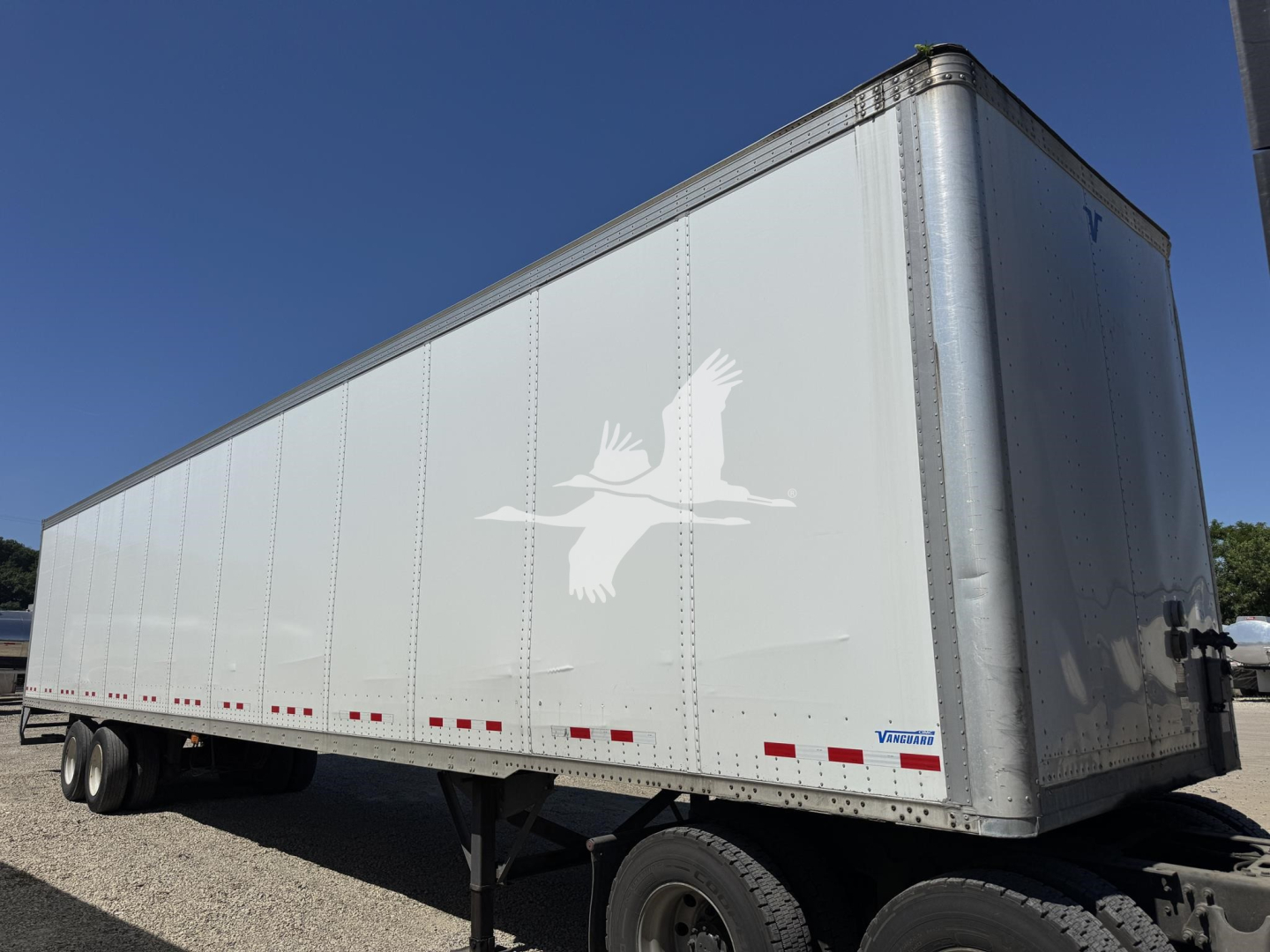 Trailer side view showing a white Vanguard VXP dry van trailer with branding and rear door, VIN plate area not visible, stock number 7724, in a yard.