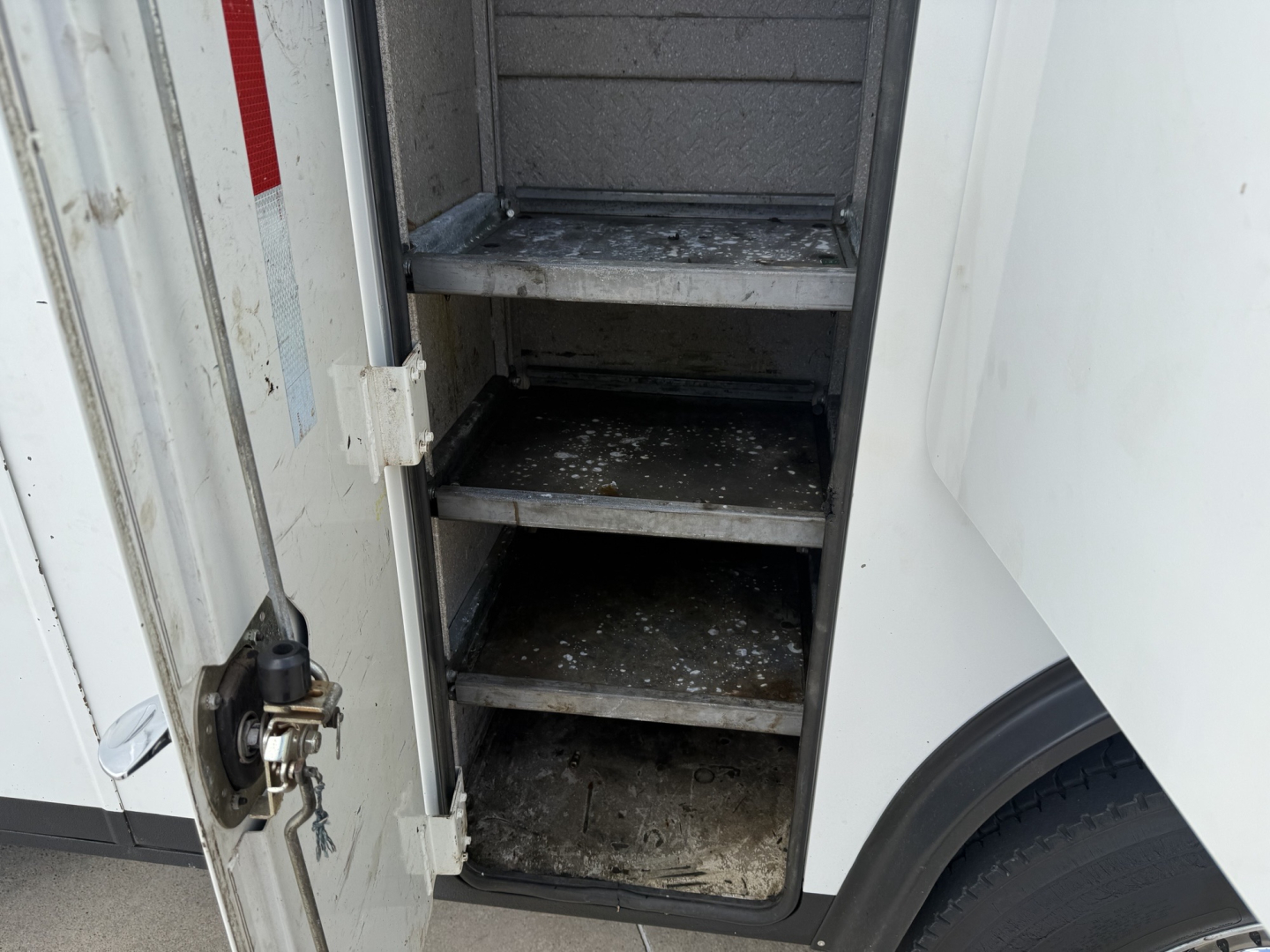 Service/Utility truck door compartment with multiple shelves inside, metal steps and dirty lower shelf in the open storage area.