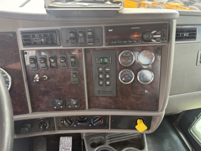 Kenworth T270 dashboard panel showing switches, gauges, and gear selector with wood-grain trim and yellow ignition key.