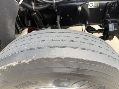 Truck wheel and undercarriage with tire tread and chassis visible; no legible text other than faint markings on tire.