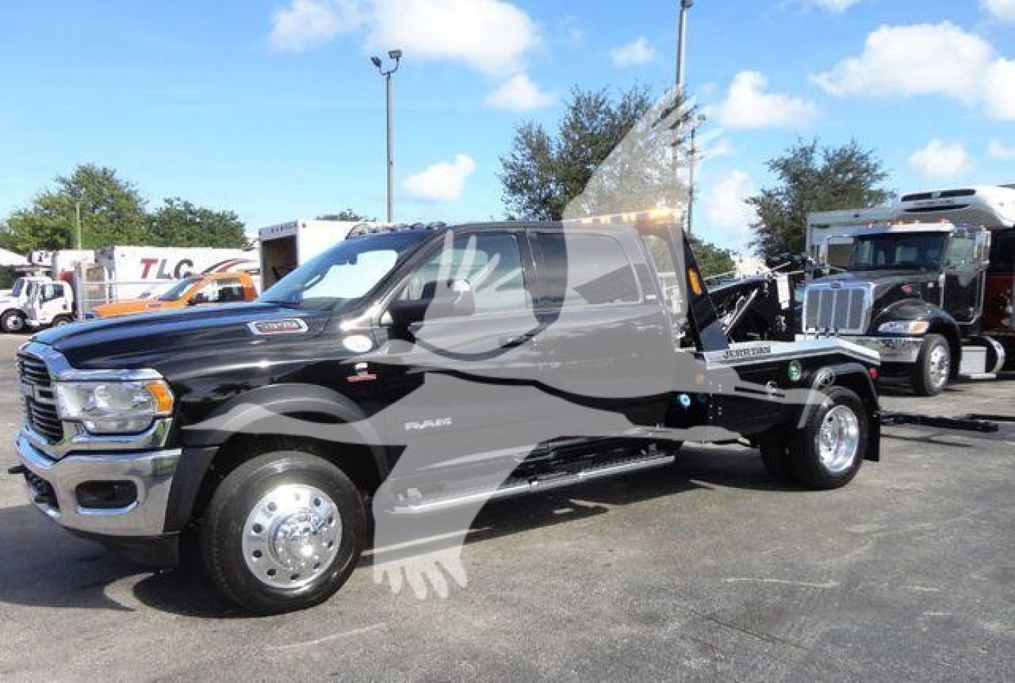 Ram 5500 tow truck chassis cab in black with dual rear wheels and flatbed, front grille, hood emblem, and dealer lot in background.