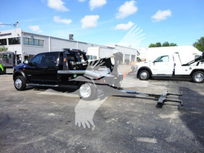 Ram 5500 tow truck with long tow assembly and winch in a dealership lot. Visible text on vehicle includes no identifiable model text; general components visible include truck cab, flatbed with tow apparatus, and background of other trucks.