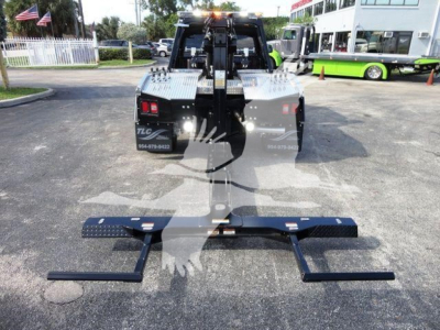 Ram 5500 tow/winch/loader rear view showing heavy-duty winch rack and bumper, with two black steel side bars extended underneath and reflective taillights.