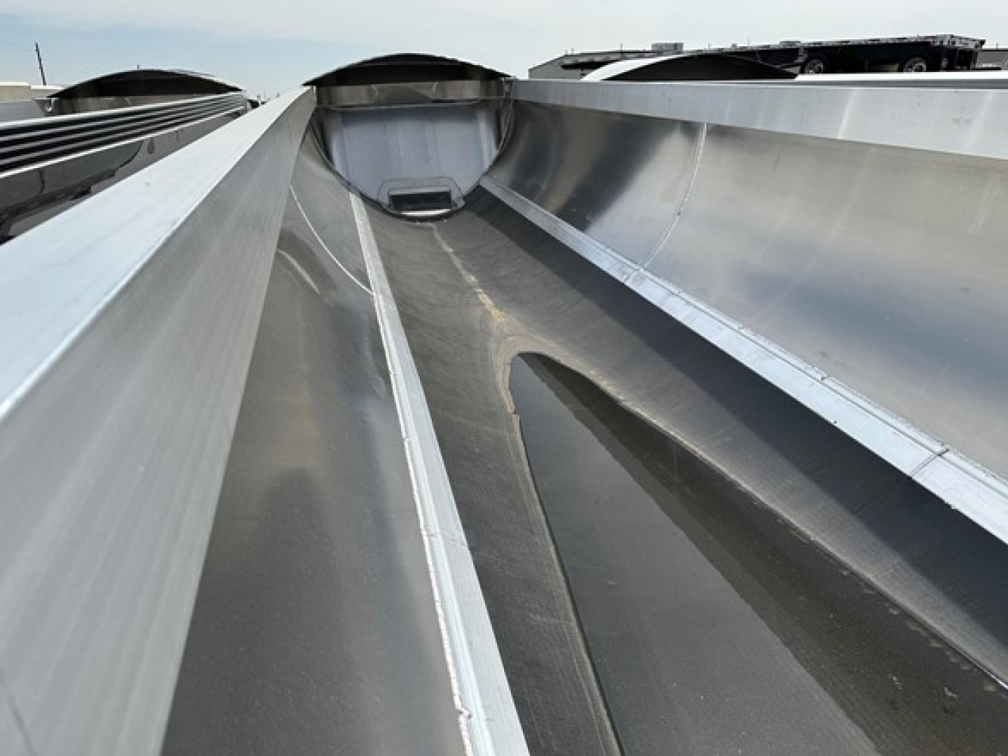 Dump trailer interior showing reinforced steel wells and center trough for material flow inside upper deck.