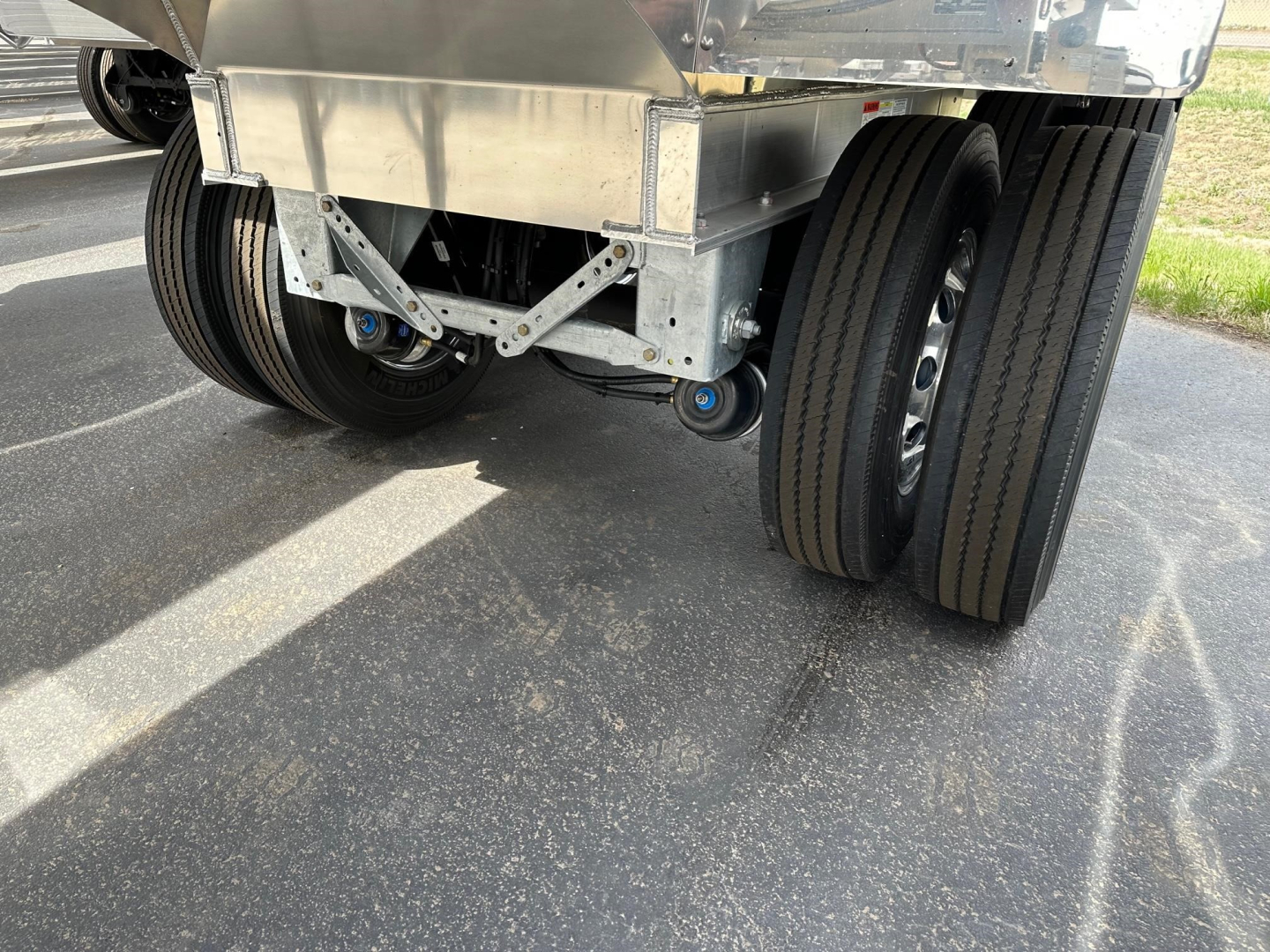 Dump trailer rear showing dual rear axles with black tires and metal suspension components under elevated hopper.