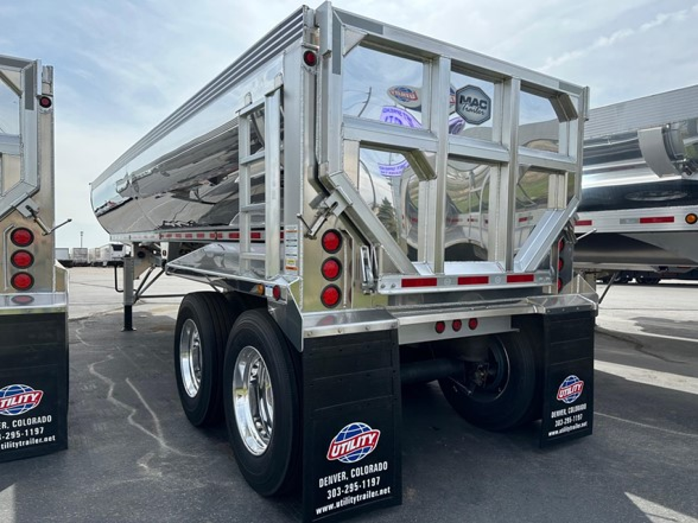 Dump trailer rear/side view showing dual-axle chrome wheels, reflective safety rails, and tail lights; MAC Macsimiser branding may be on the rear gate.