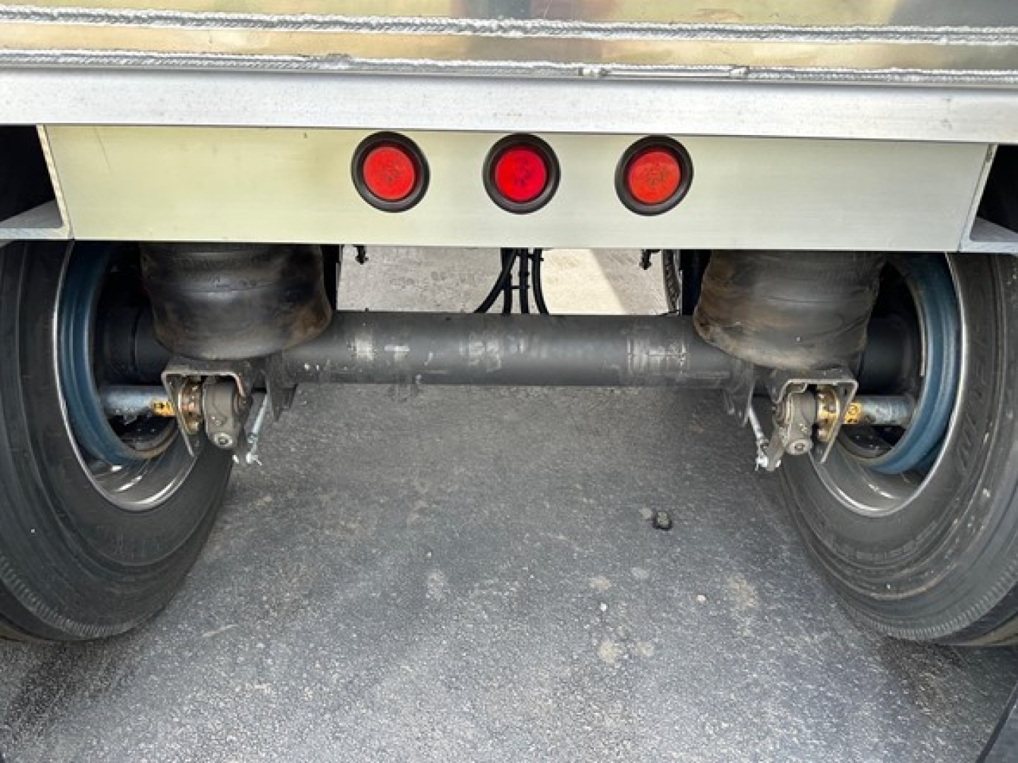 Rear view of Mac Macsimiser dump trailer showing dual wheels and suspension with three red taillights visible.