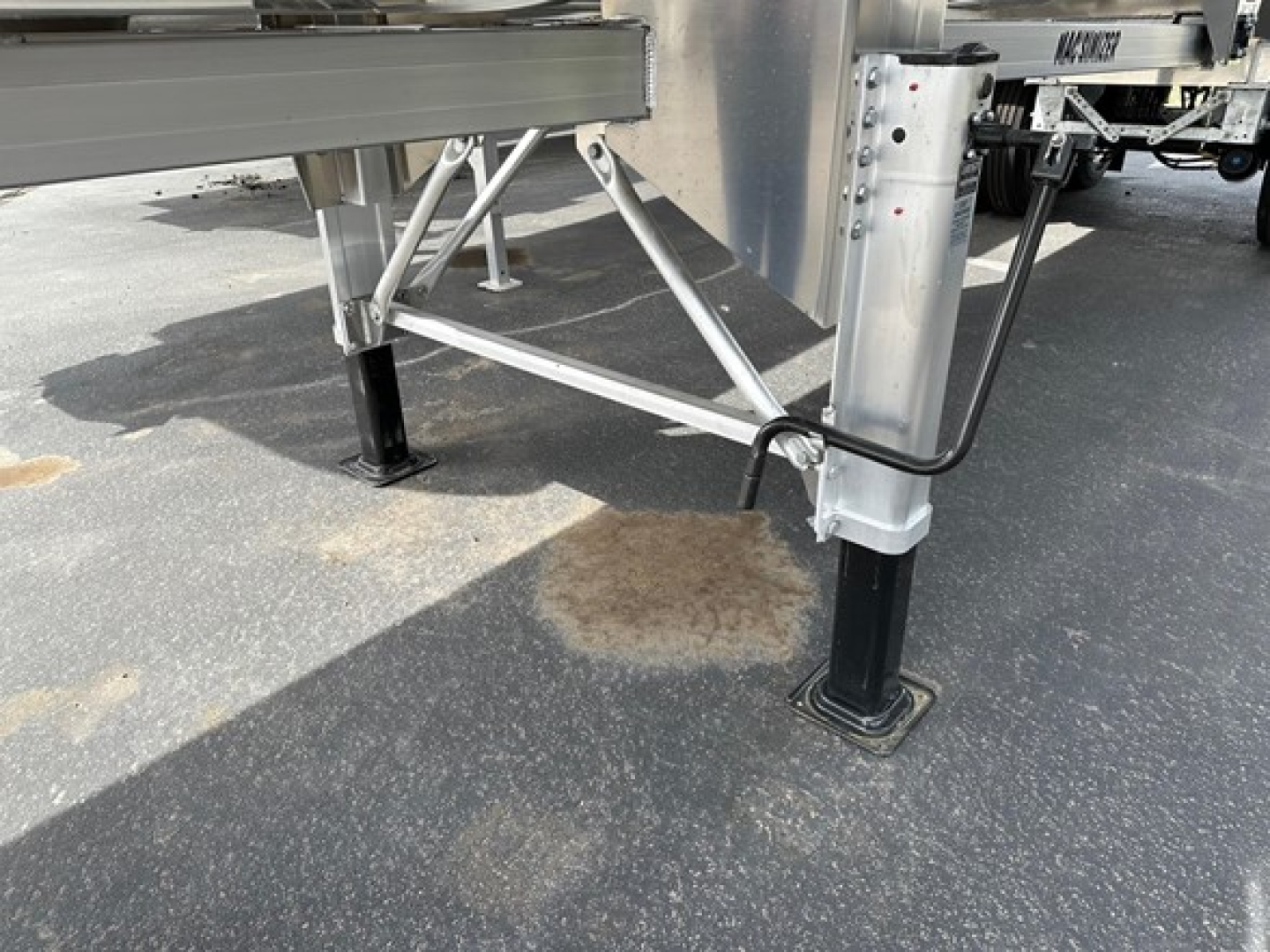 Mac Macsimiser trailer leg and frame details showing level landing gear and support legs on concrete with hydraulic lines and metal support brackets.
