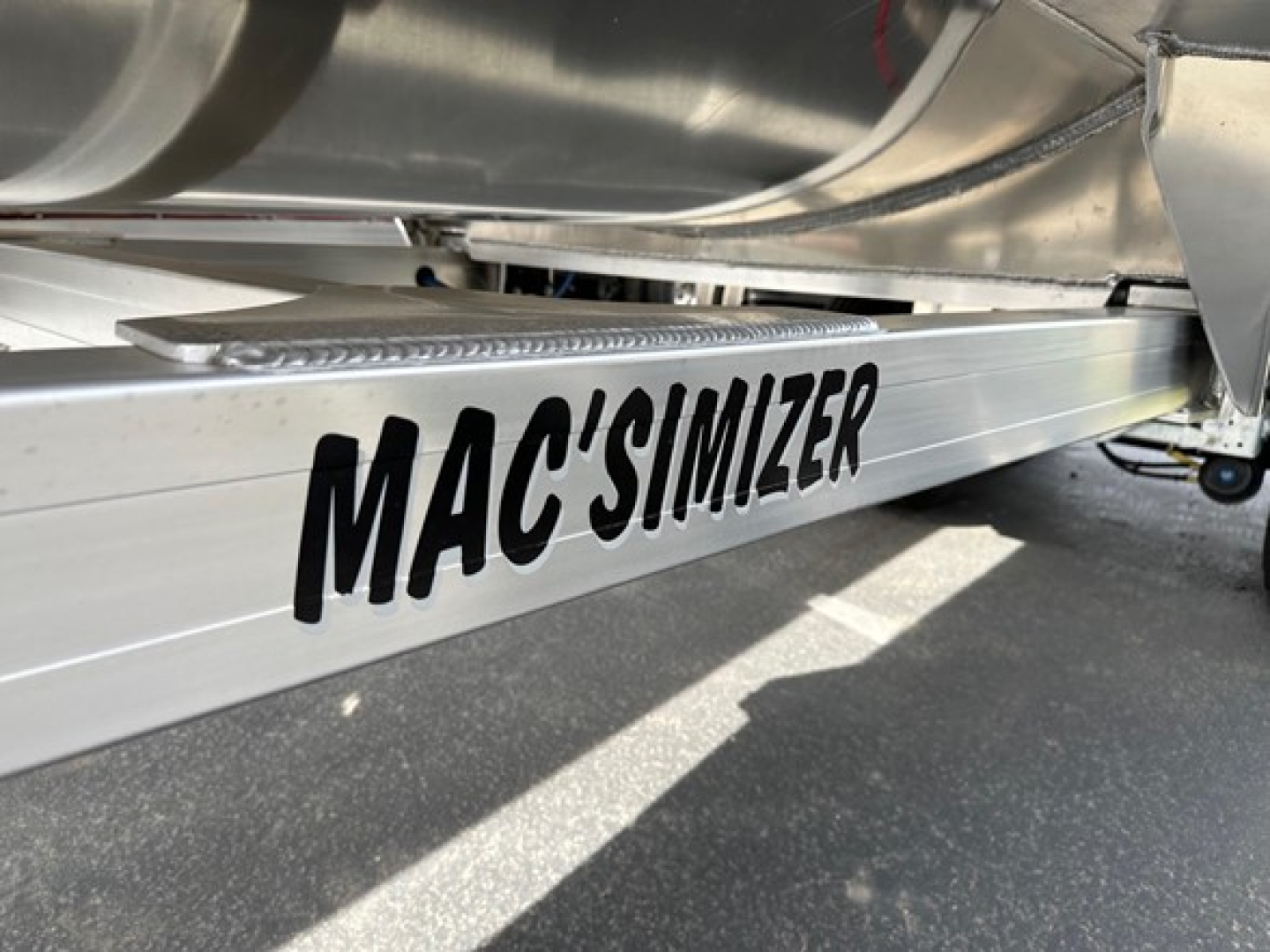 Mac'simizer aluminum trailer side rail with bold black MAC'SIMIZER text; metallic components and undercarriage visible.