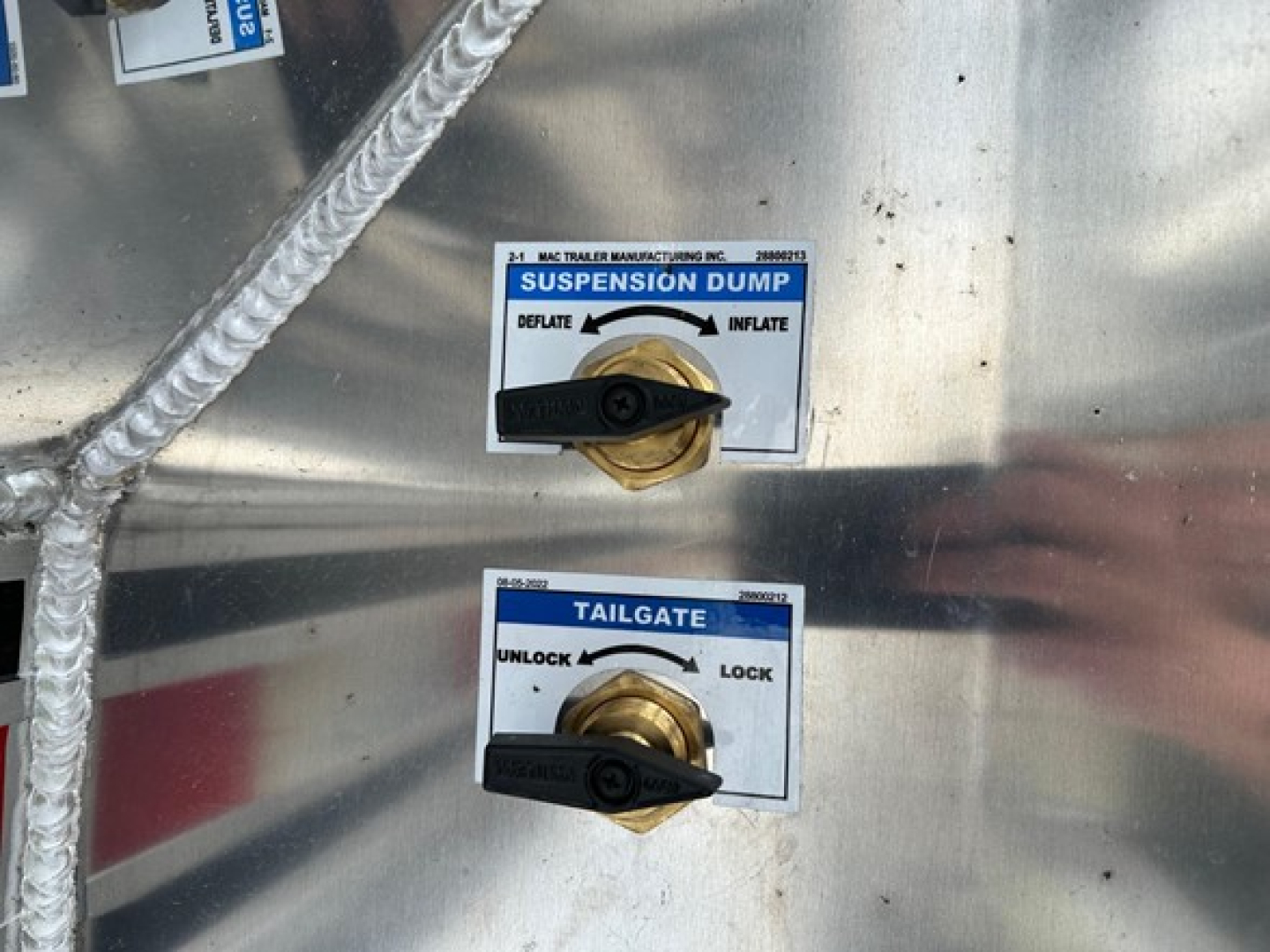 Suspension dump and tailgate control levers on a metal trailer surface with labeled blue/white decals.