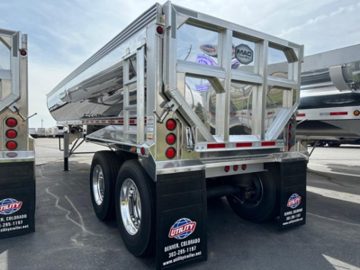 Dump trailer rear/side view showing dual-axle chrome wheels, reflective safety rails, and tail lights; MAC Macsimiser branding may be on the rear gate.