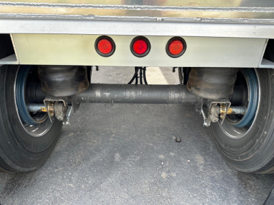Trailer rear underside showing tandem axles, heavy-duty differential beam, and red LED tail lights.