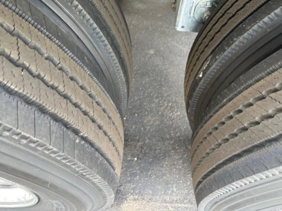Dual truck tires mounted on a trailer with a textured asphalt surface between them. Visible tread patterns on both left and right tires.