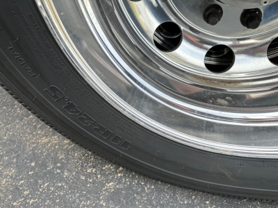 Trailer wheel/tire close-up showing chrome rim and black tire with text  