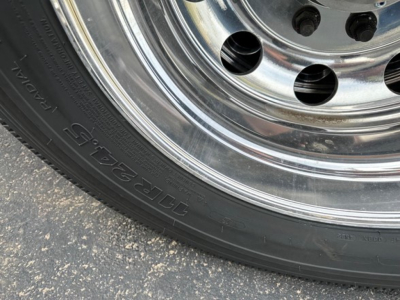 Wheel and tire close-up on a trailer showing a polished chrome rim and a black radial tire with embossed text on the sidewall.