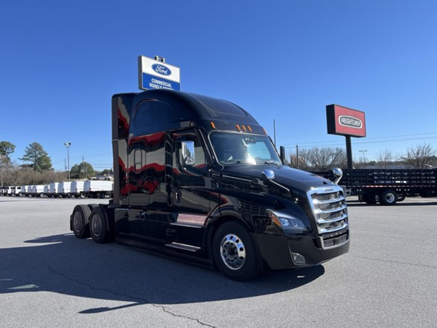 Freightliner Cascadia 126 tractor in a dealership lot, black paint, three-axle sleeper configuration, front grille, side mirrors, and skyline exhaust, new unit.