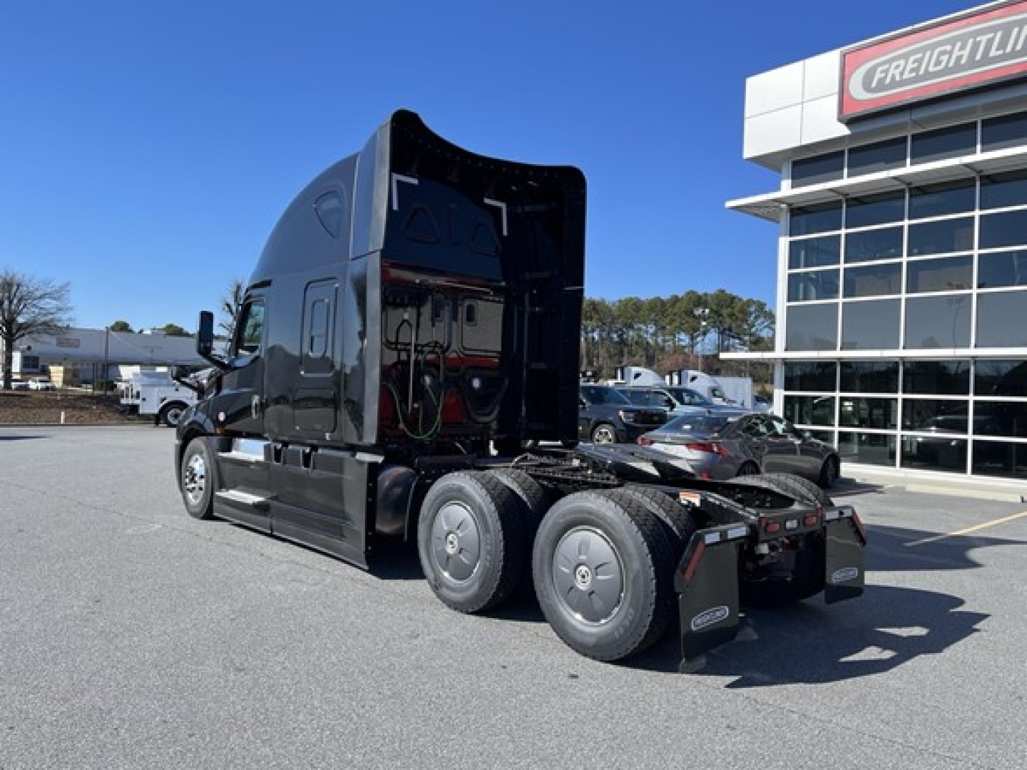 New Freightliner Cascadia 126 semi truck in a dealership lot showing a sleeper cab and rear axles.