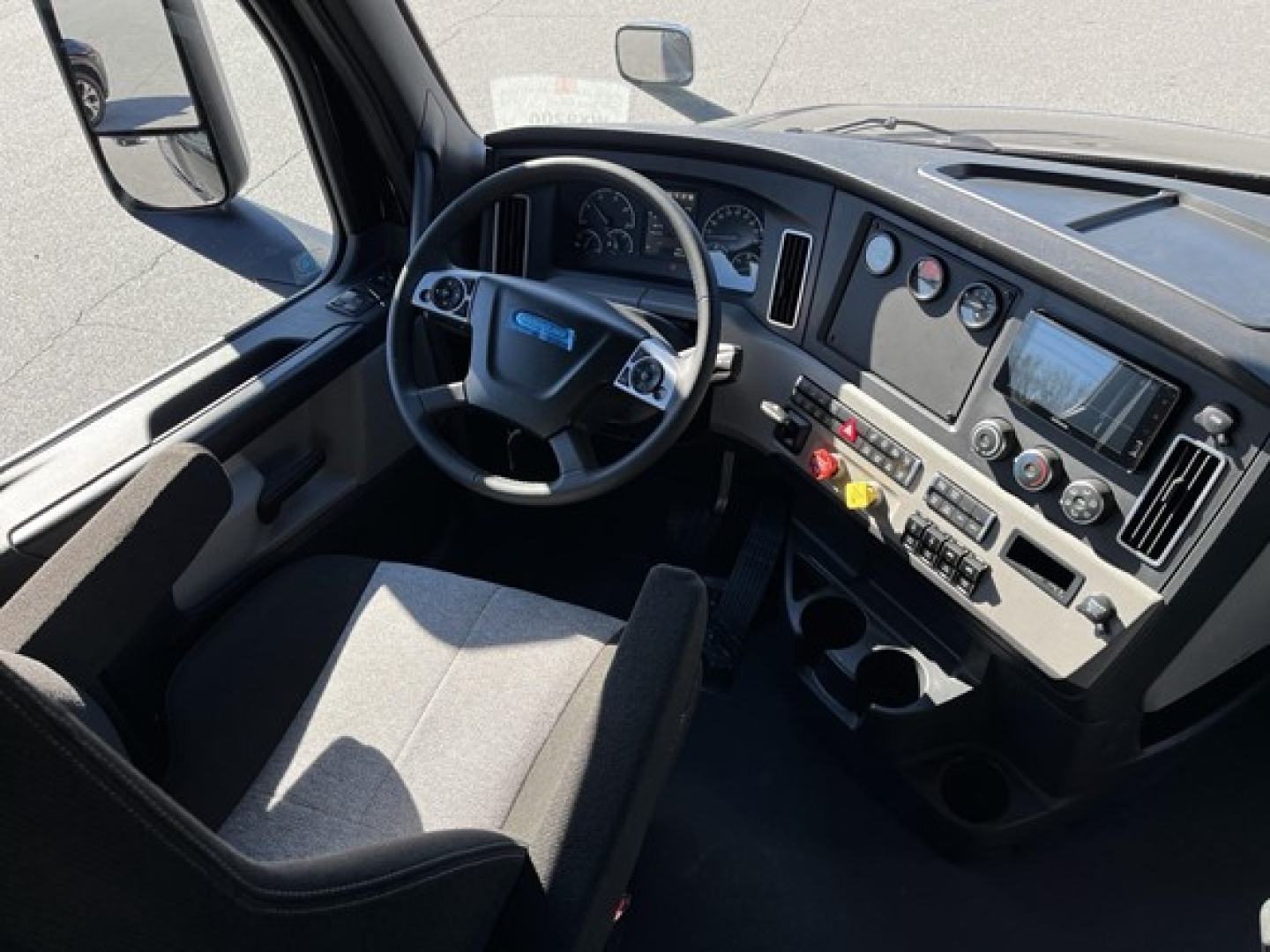 Freightliner Cascadia truck cab interior seen from driver seat showing steering wheel, dashboard gauges, and center console panels.
