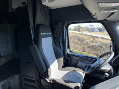Truck cab interior showing driver seat with 'CASCADIA' logo, steering wheel, dashboard, and window.