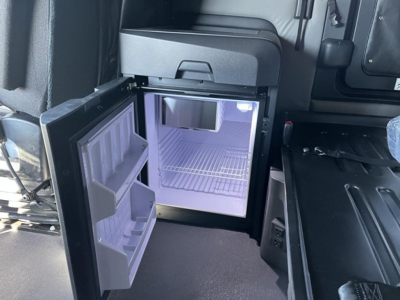 Freightliner Cascadia cab interior showing open mini fridge/freezer with shelves and empty freezer compartment.