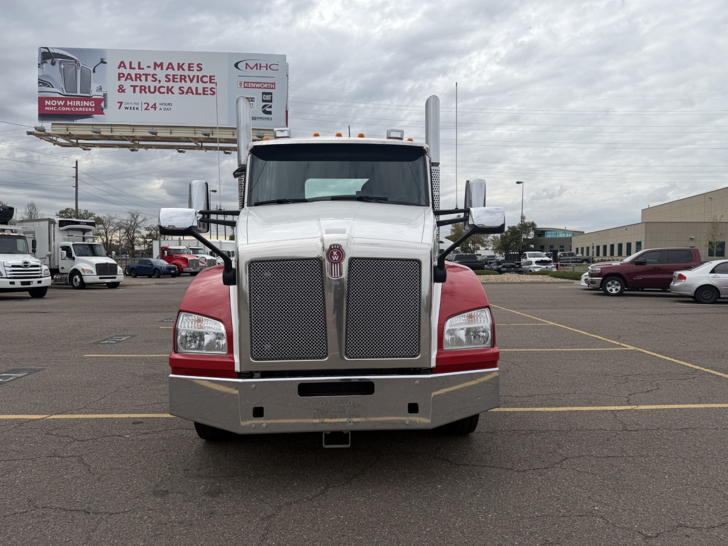 Kenworth T880 front view with large chrome grille and dual headlights, white cab with red lower fenders; billboard in background reads ALL MAKES PARTS, SERVICE & TRUCK SALES.