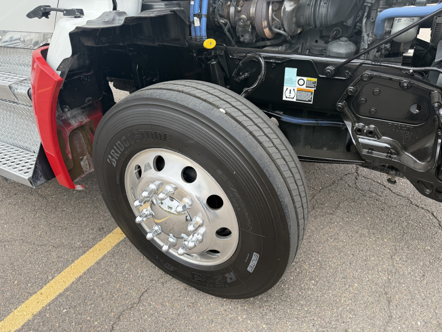 Kenworth T880 front wheel assembly showing Bridgestone tire and wheel with hub, engine bay and chassis components visible.