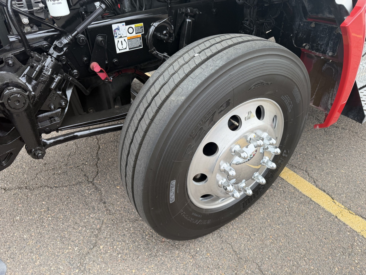 Kenworth T880 front wheel and suspension detail showing heavy-duty dual axle with silver hub, lug nuts, and black undercarriage components.