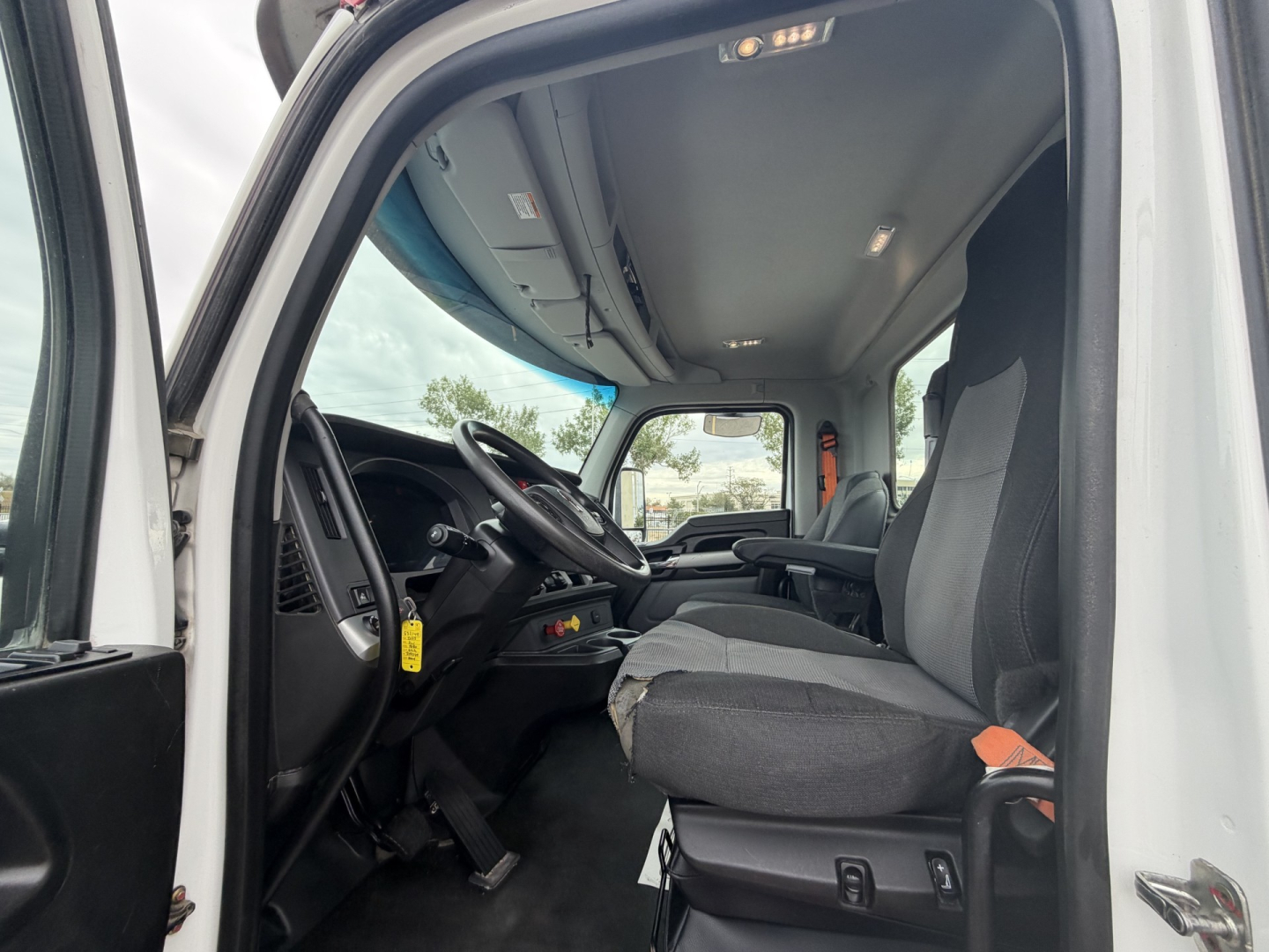 Kenworth T880 cab interior showing steering wheel, driver seat, dashboard, and front door area; overhead light and windows visible.