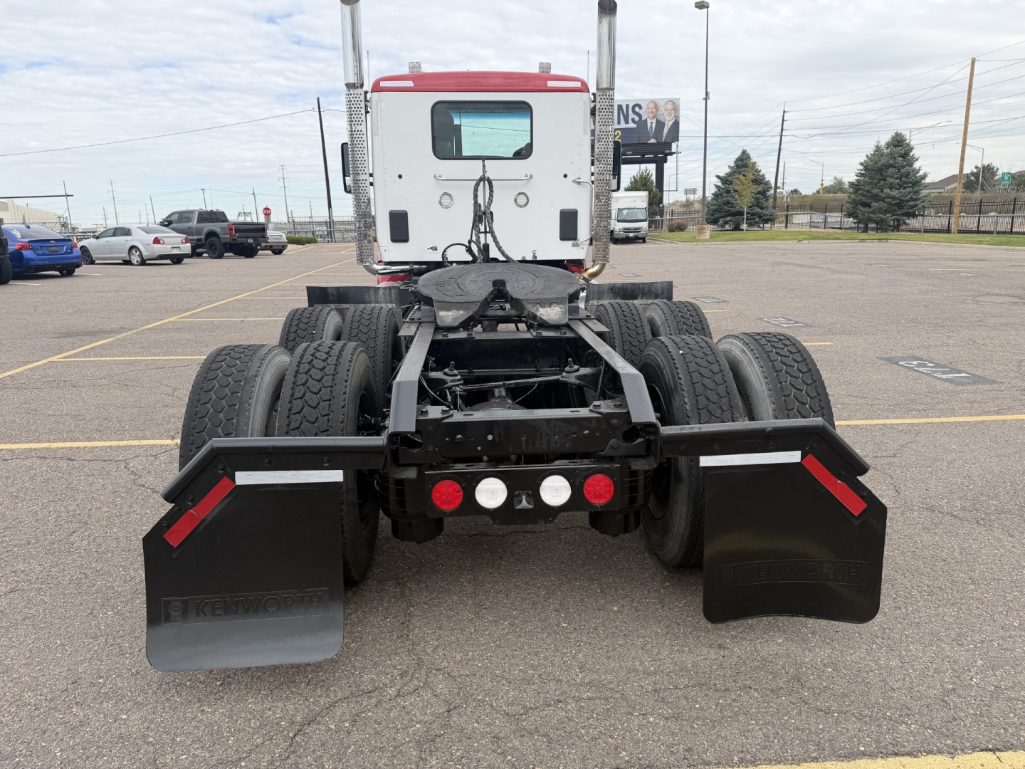 Kenworth T880 chassis rear view showing dual rear axles, black mud flaps, and bumper with red reflectors; cab in background, VIN plate area not visible.
