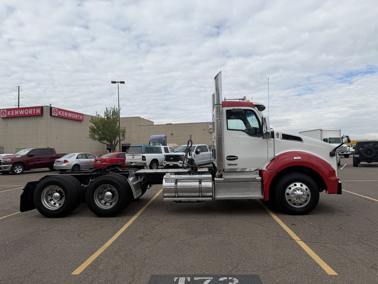 Kenworth T880 truck in a parking lot, side view showing cab with red front and chrome fuel tanks, dual rear axles, standard sleeper cab door.