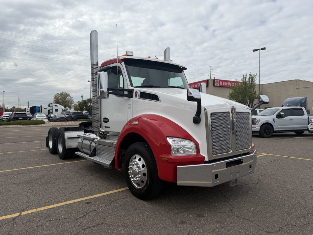 Kenworth T880 conventional daycab truck in white and red, front left side view with chrome grille and dual exhaust stacks.
