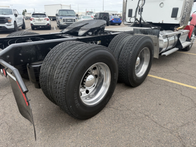 Kenworth T880 truck chassis showing rear dual axles and dual rear tires with chrome rims, fuel tanks, and cab in the distance.