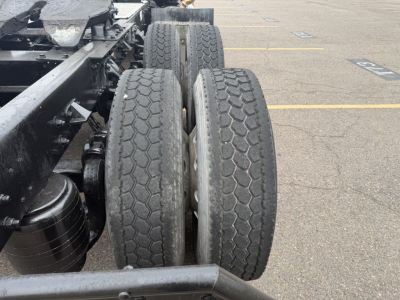 Kenworth T880 chassis showing dual rear axles with worn tread on tires and wheel rims; visible universal components and frame in a parking lot.