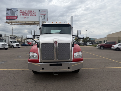 Kenworth T880 front view with large chrome grille and dual headlights, white cab with red lower fenders; billboard in background reads ALL MAKES PARTS, SERVICE & TRUCK SALES.