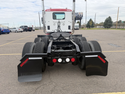 Kenworth T880 chassis rear view showing dual rear axles, black mud flaps, and bumper with red reflectors; cab in background, VIN plate area not visible.