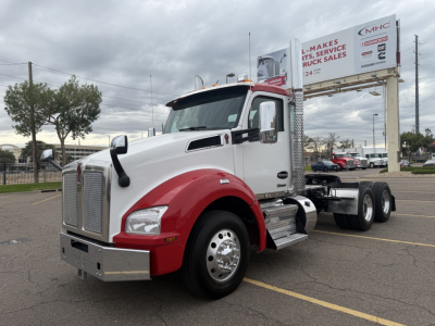 Kenworth T880 cab in white and red with dual rear axles, showing front grille, headlights, chrome bumper, and side mirror. Large sign in background reads 'MHC Makes It Happen Service Truck Sales'.